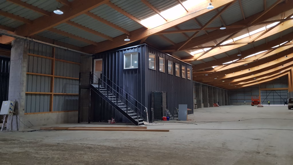 Fotografía del interior de la bodega principal de SQM, mostrando la estructura de madera laminada del techo y las oficinas internas construidas con contenedores.