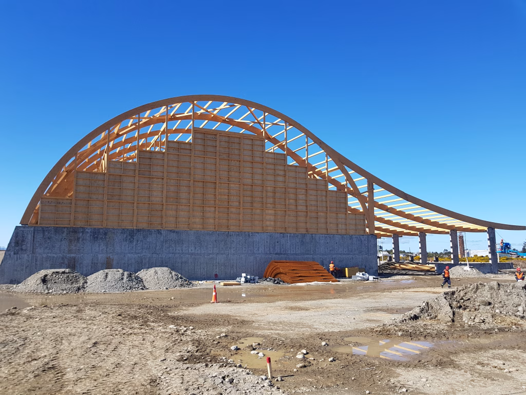 Fotografía de la estructura de madera laminada de la bodega SQM vista lateralmente, mostrando los muros de contención de hormigón y el inicio de la curvatura del techo.